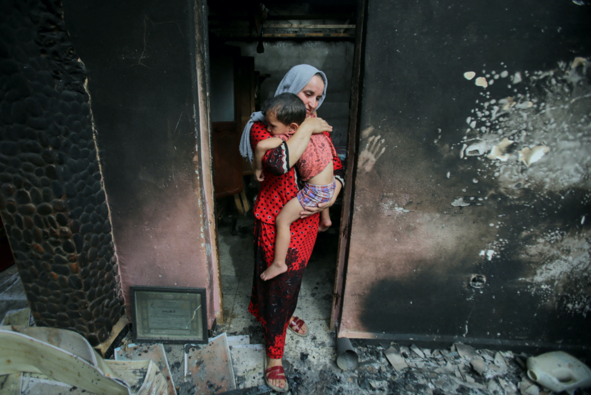 Souhila Belkati carries her child inside her burnt house following a wildfire in Bejaia, Algeria, on 25th July, 2023.