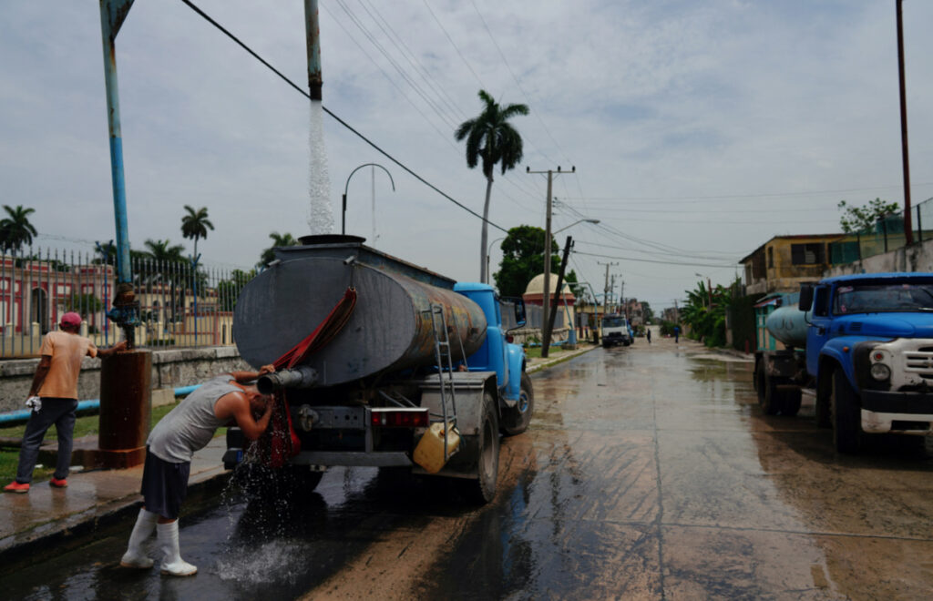 A driver refreshes himself as he fills up the tank of a water truck in Havana, Cuba, on 3rd July, 2023