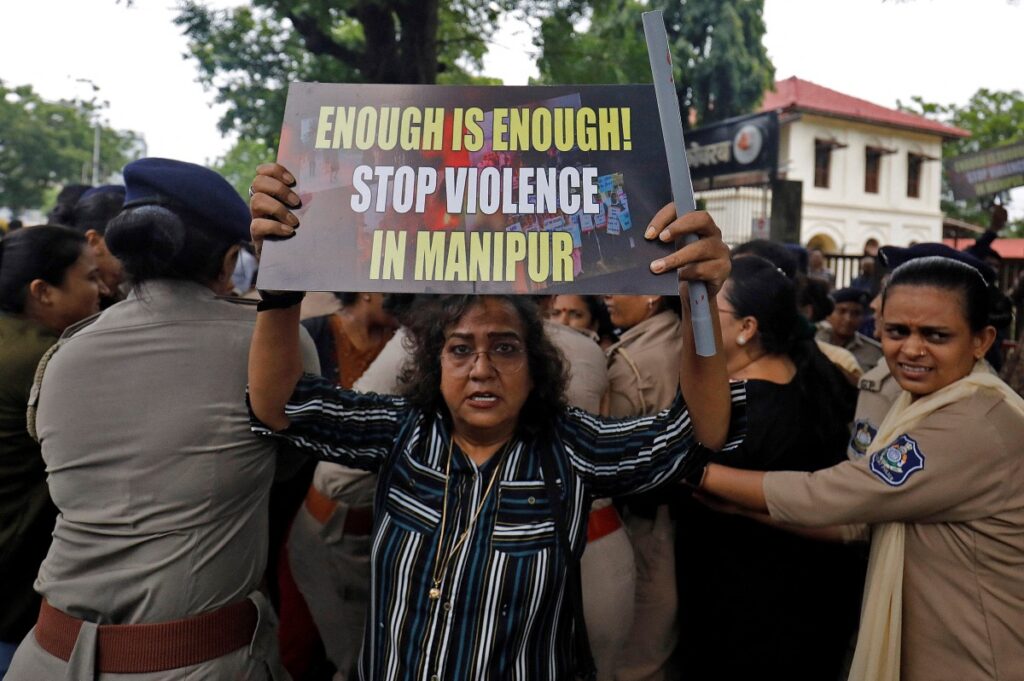 A demonstrator holds up a placard, as police officers detain others during a protest against the alleged sexual assault of two tribal women in the eastern state of Manipur, in Ahmedabad, India, on 23rd July, 2023.