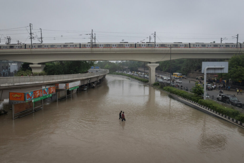Men walk across a road flooded due to the high water level of the river Yamuna after heavy monsoon rains, New Delhi, India, on 13th July, 2023.