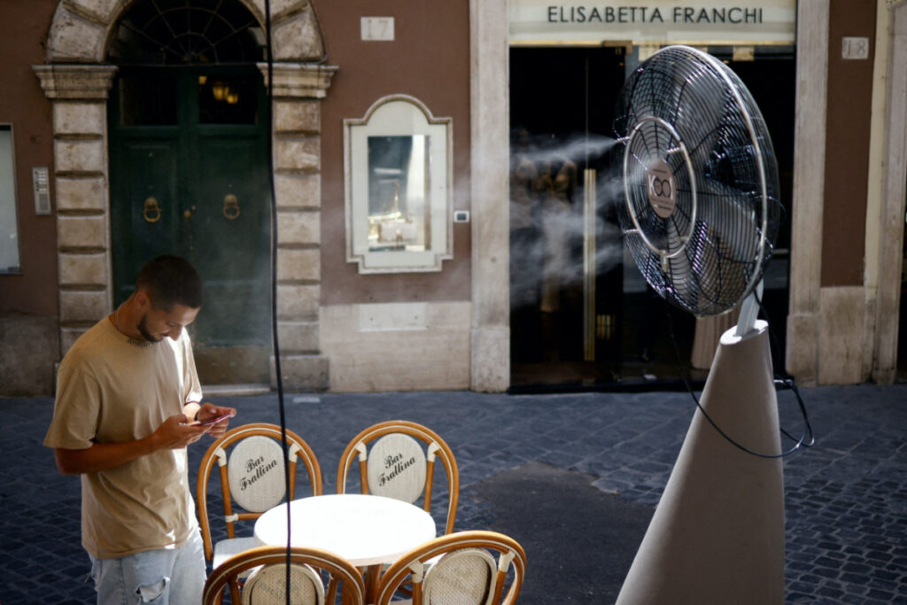 A man checks his phone as he stands near a fan to cool off during a heatwave across Italy, in Rome, on 14th July, 2023