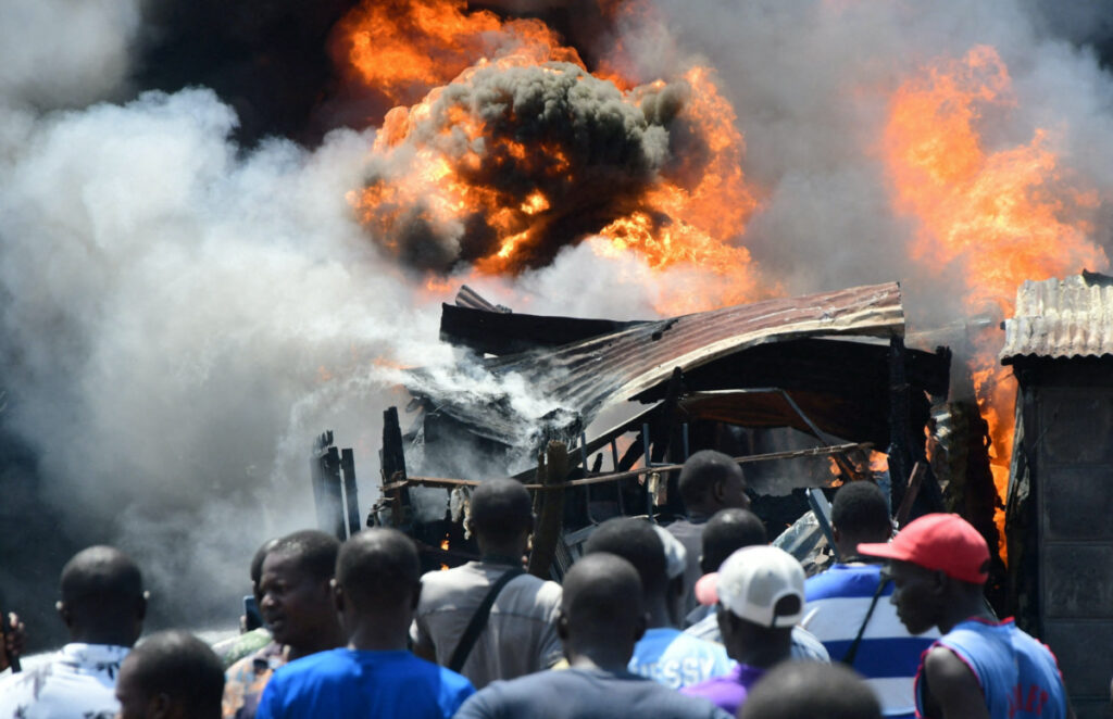 People gather near burning business premises after supporters of Kenya's opposition leader Raila Odinga of the Azimio La Umoja One Kenya Alliance, clashed with riot police officers as they participated in an anti-government protest against the imposition of tax hikes by the government, in Kisumu county, Kenya, on 19th July, 2023