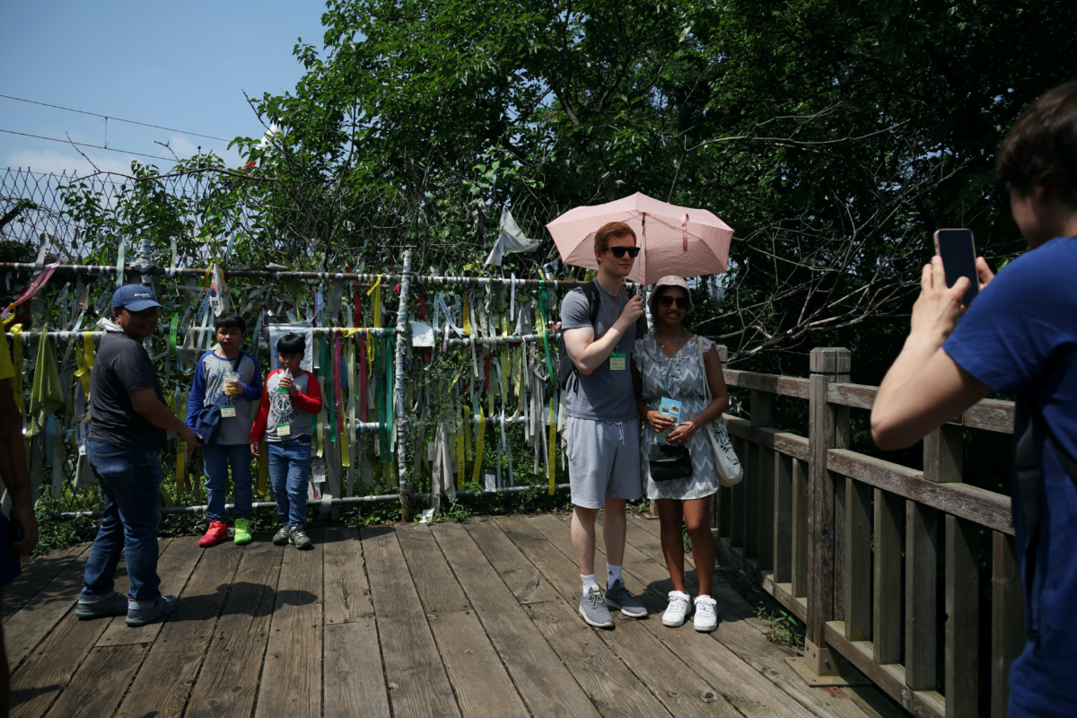 Foreign tourists participating in DMZ tour pose for photographs in front of a military fence near the demilitarized zone separating the two Koreas, in Paju, South Korea, on 19th July, 2023.  