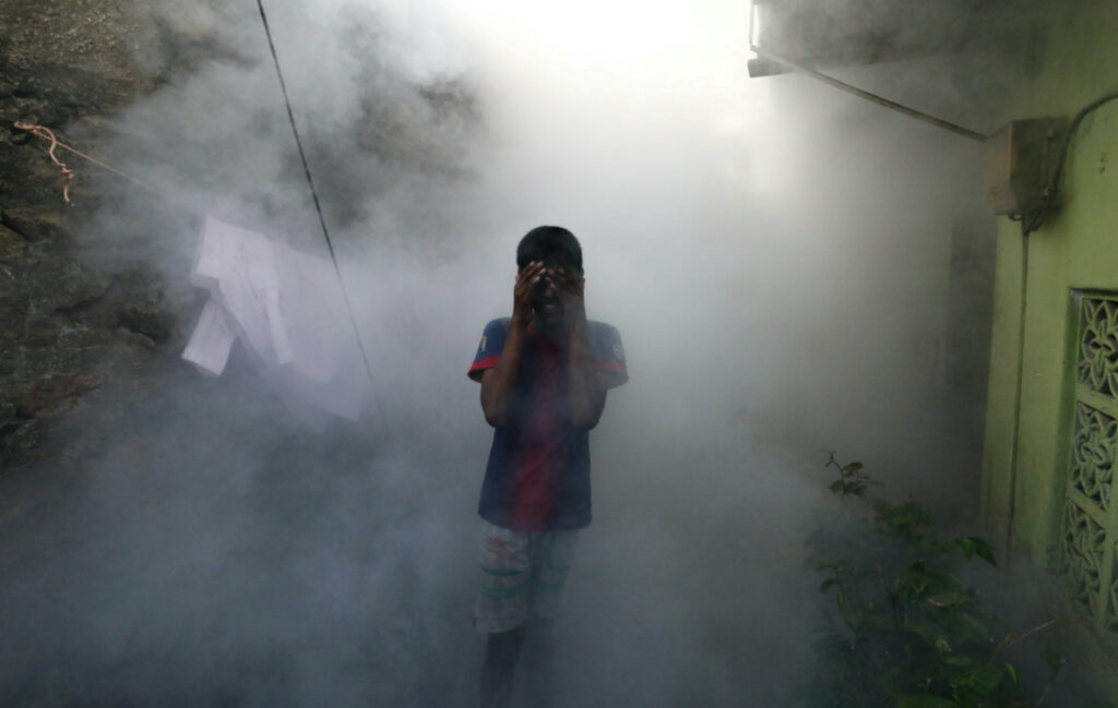 A boy covers his face from smoke as a health worker fumigates against mosquitoes in a residential area, as Sri Lanka tries to curb dengue fever across the island in Colombo, Sri Lanka, on 12th July, 2023.