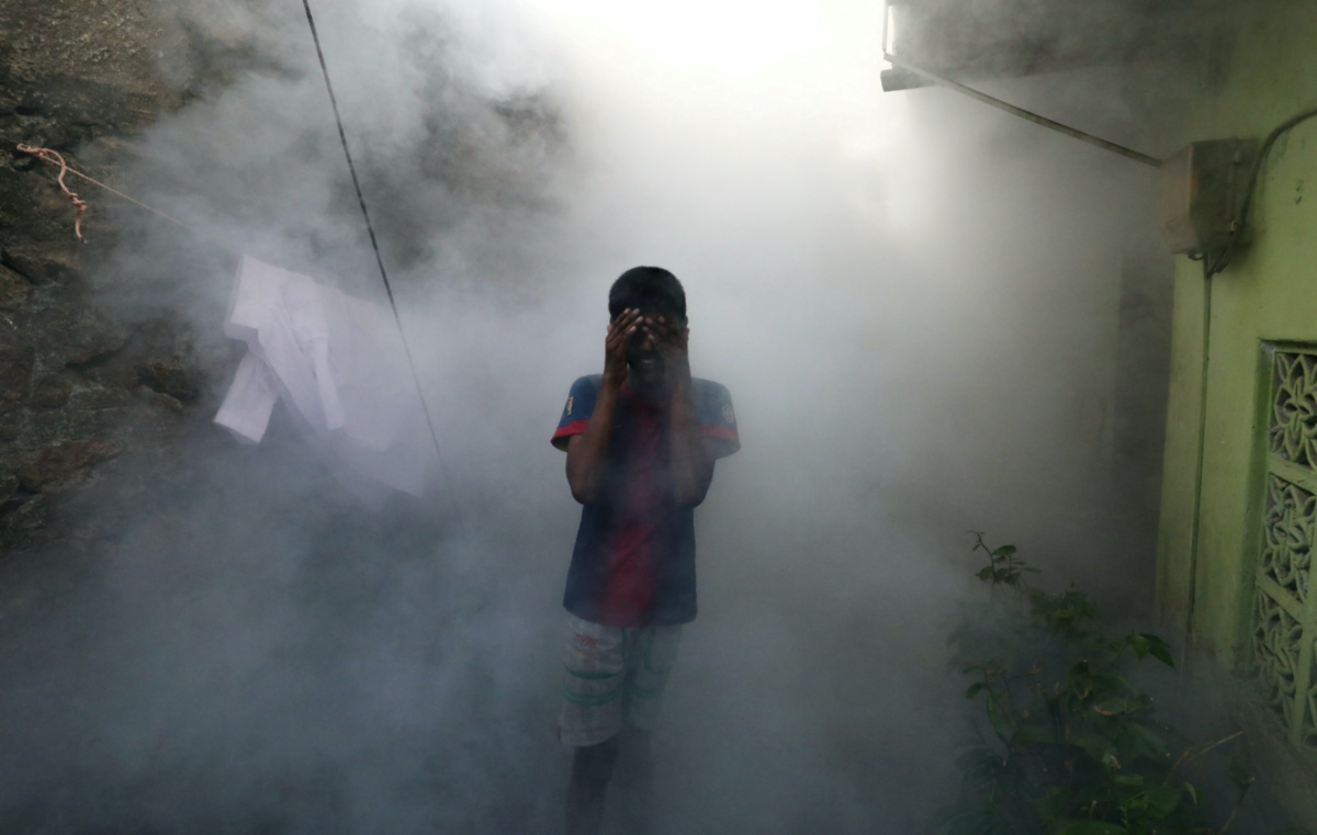A boy covers his face from smoke as a health worker fumigates against mosquitoes in a residential area, as Sri Lanka tries to curb dengue fever across the island in Colombo, Sri Lanka, on 12th July, 2023. 