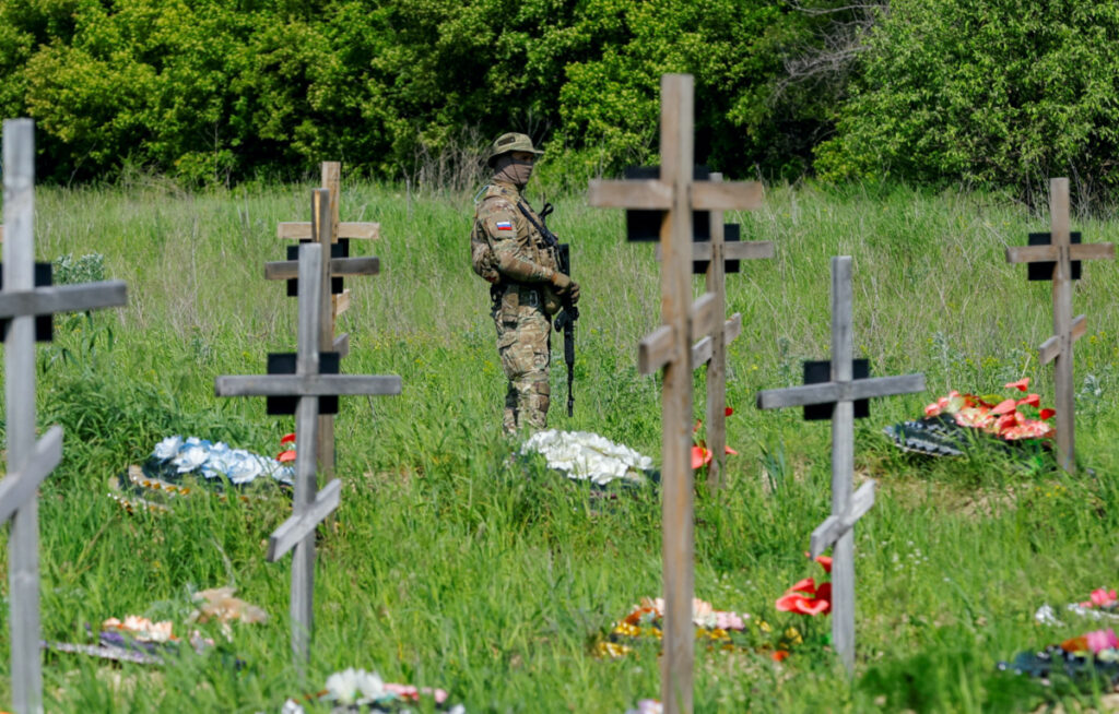 An armed soldier stands guard during a funeral ceremony to bury the remains of sixty service members of the Russian armed forces and three civilians, who were killed in the course of Russia-Ukraine conflict, at a cemetery in Luhansk, Russian-controlled Ukraine, on 18th May, 2023.