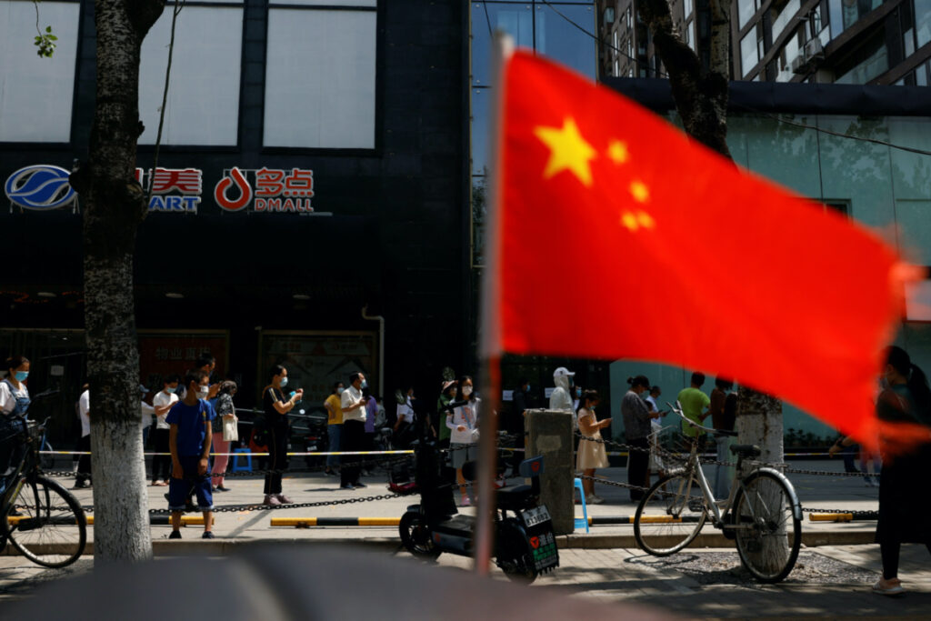 A China's flag flutters near people lining up to get tested at a makeshift nucleic acid testing site, amid the coronavirus disease outbreak in Beijing, China on 18th May, 2022