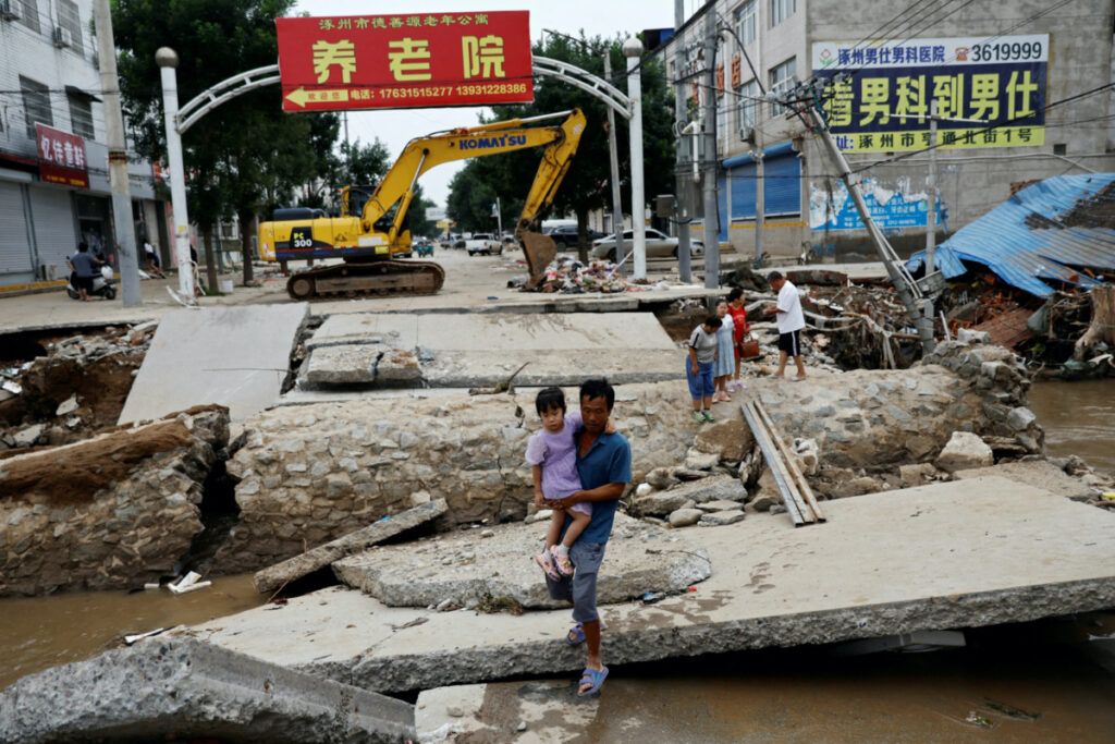 A man holding a child walks across a damaged bridge after the rains and floods brought by remnants of Typhoon Doksuri, in Zhuozhou, Hebei province, China, on 7th August, 2023.