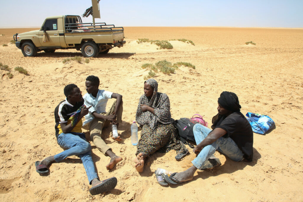 Tafaul Omar, a pregnant 26-year-old nurse from Sudan, talks to a group of men as she is stranded in the desert on the Libyan-Tunisian border, near Al-Assah, Libya, on 5th August, 2023.