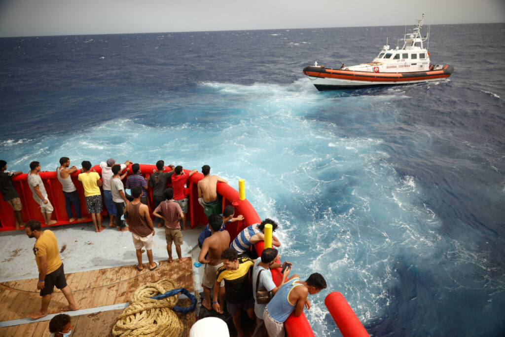 Migrants on board of NGO Proactiva Open Arms Uno rescue boat looks at boat Guardia Costiera heading to Lampedusa island, in central Mediterranean Sea, close to Lampedusa island, Italy, on 19th August, 2022.