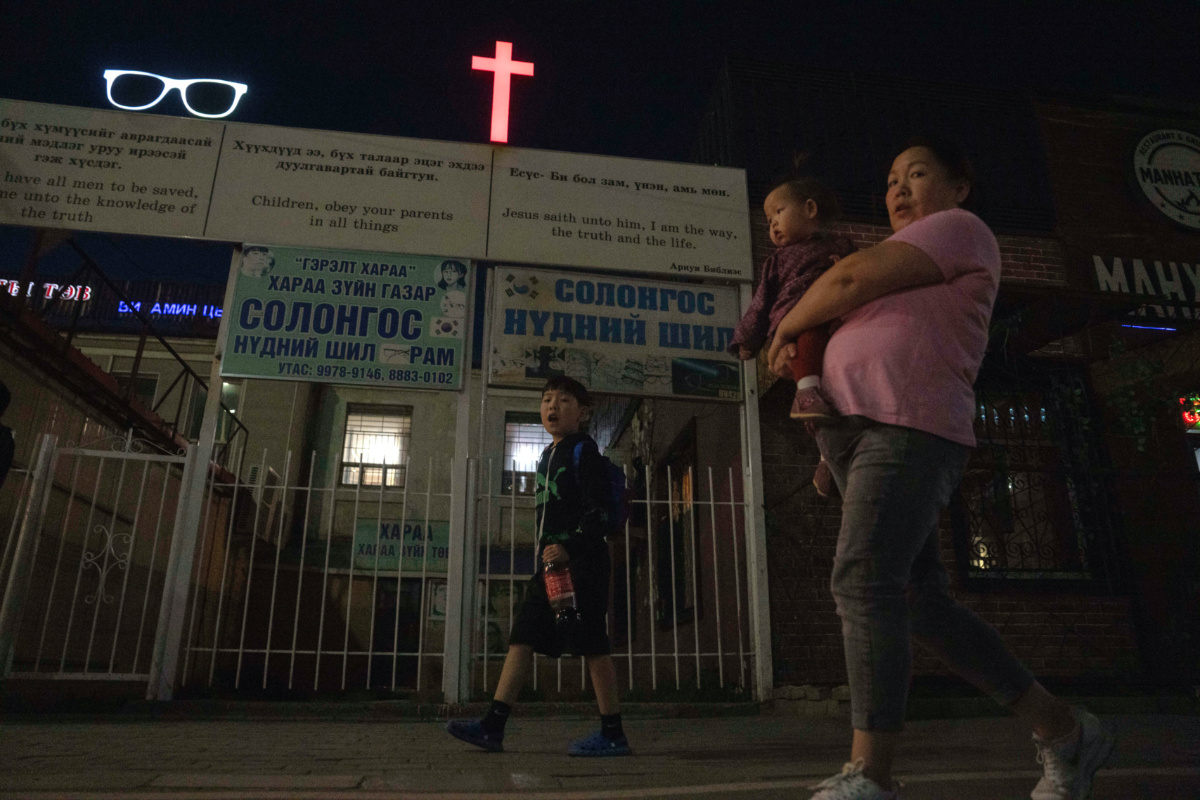 A woman carries a child past a cross and Christian quotes on the street in Ulaanbaatar, Mongolia on Tuesday, 29th August, 2023.