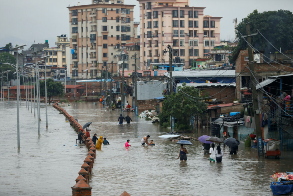 People walk along a flooded road along the bank of overflowing Bagmati river following heavy rains, in Kathmandu, Nepal, on 8th August, 2023.