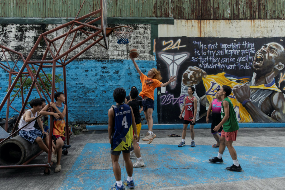Teenagers play basketball at a court in front of a mural of Kobe Bryant in Manila, Philippines, on 17th July, 2023