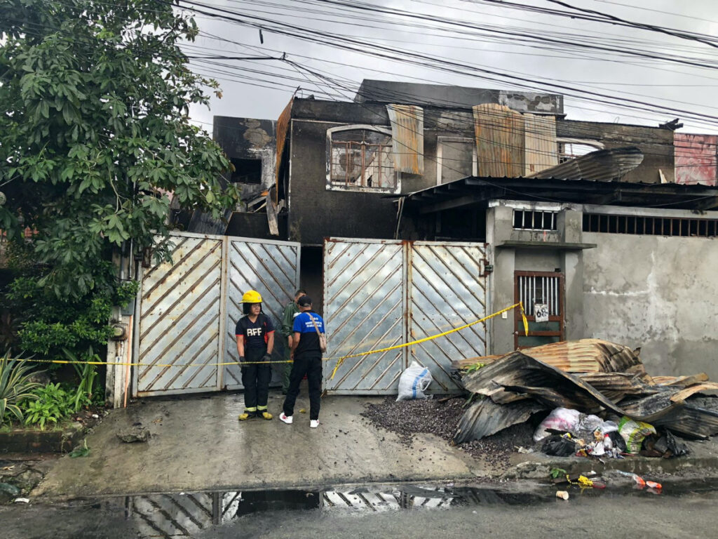 Rescuers and village officials stand in front of a burnt residential building after it was engulfed in a fire in Quezon City, Metro Manila, Philippines, on 31st August, 2023