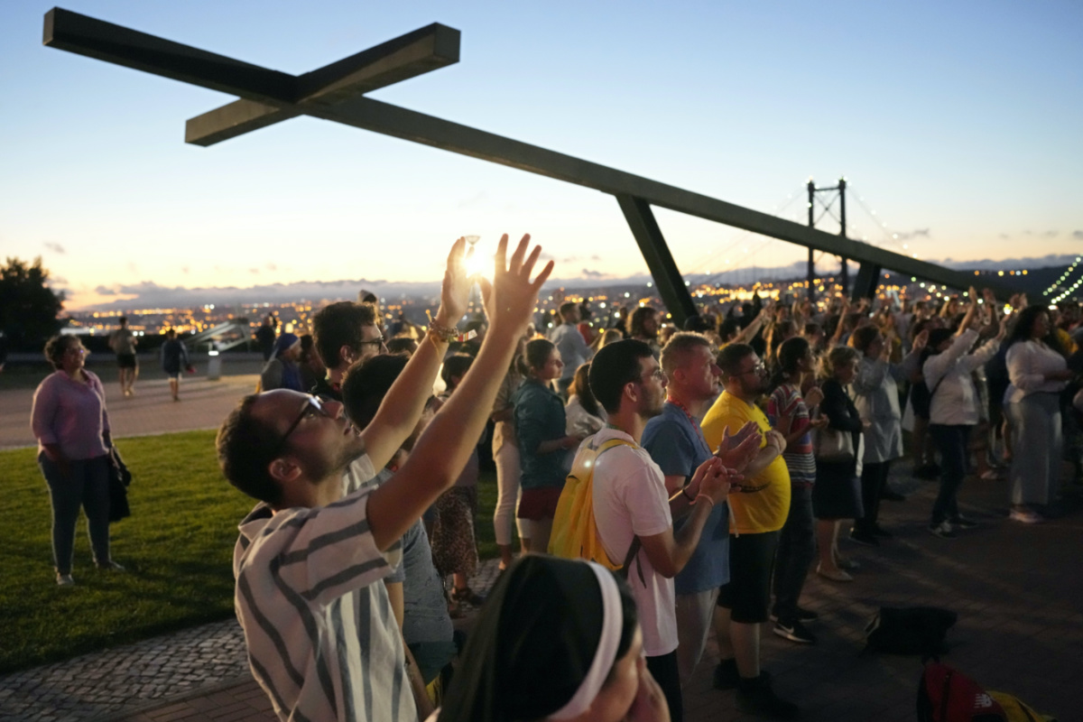 Faithful sing Christian songs before a vigil attended by people arriving early for the World Youth Day at a viewpoint overlooking Lisbon from across the Tagus River, in Almada, Portugal, as night falls, on Friday, 28th July, 2023.