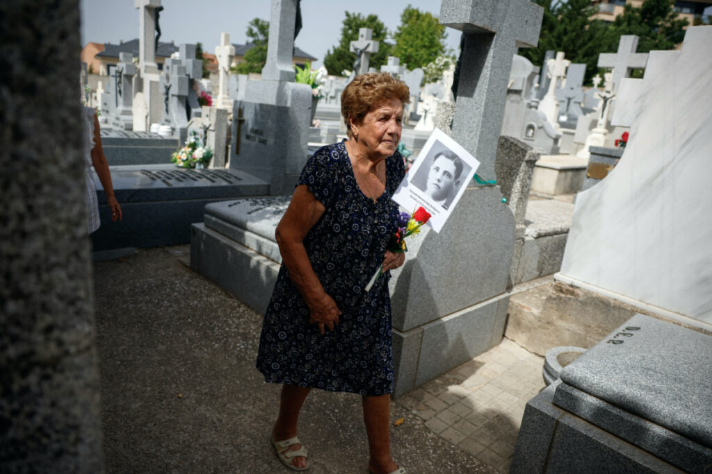 Benita Navacerrada Lopez walks as she holds a picture of her father Facundo Navacerrada Perdiguero who was one of the people who were killed by the forces of dictator Francisco Franco and for whom members of the Aranzadi Science Society are searching for in a mass grave in the Colmenar Viejo cemetery, Spain, on 9th August, 2023.