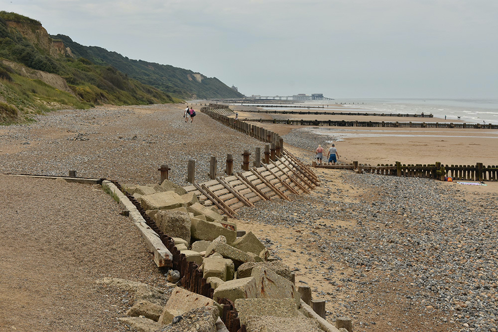 Riprap, a timber wave break, and wooden groynes protect the beach and trap sediment in Overstrand, England, on 17th June, 2023