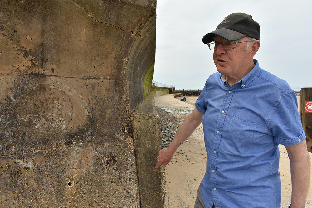 Longtime Overstrand resident Gordon Partridge points out repairs and reinforcement to the old sea wall made over the years in the small Norfolk village in England, on 17th June, 2023