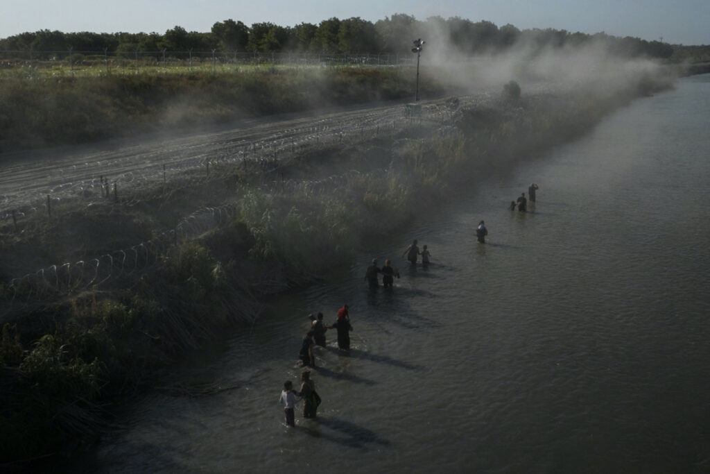 The Heavenly Farms pecan orchard is seen in the background as dust rises over migrants wading the Rio Grande river while searching for an entry point into the United States from Mexico in Eagle Pass, Texas, US, on 30th July, 2023