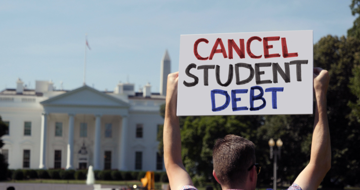 A man holds an CANCEL STUDENT DEBT protest sign in front of the White House on a sunny summer day.
