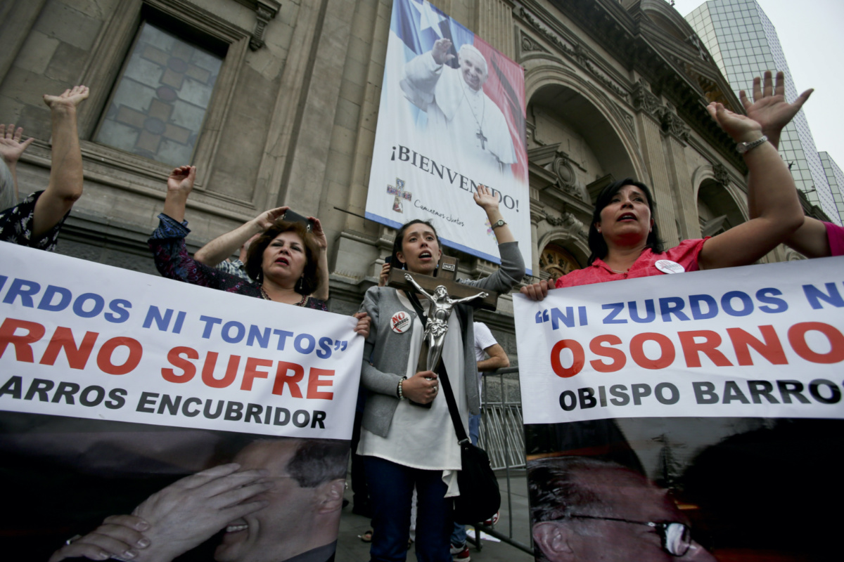 Members of the movement, Lay People of Osorno, sing as they hold images of Priest Fernando Karadima and his protege, Osorno Bishop Juan Barros, with the Spanish message: "A bishop who covers up cannot be a priest," outside the cathedral where a poster of Pope Francis hangs in Santiago, Chile, on 18th January, 2018.