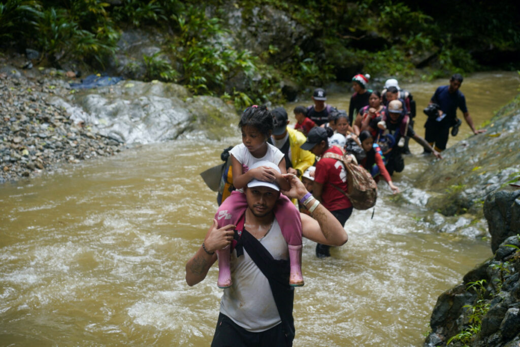 A migrant carries a child as they along with others continue their journey to the US border, in Acandi, Colombia, on 9th July, 2023
