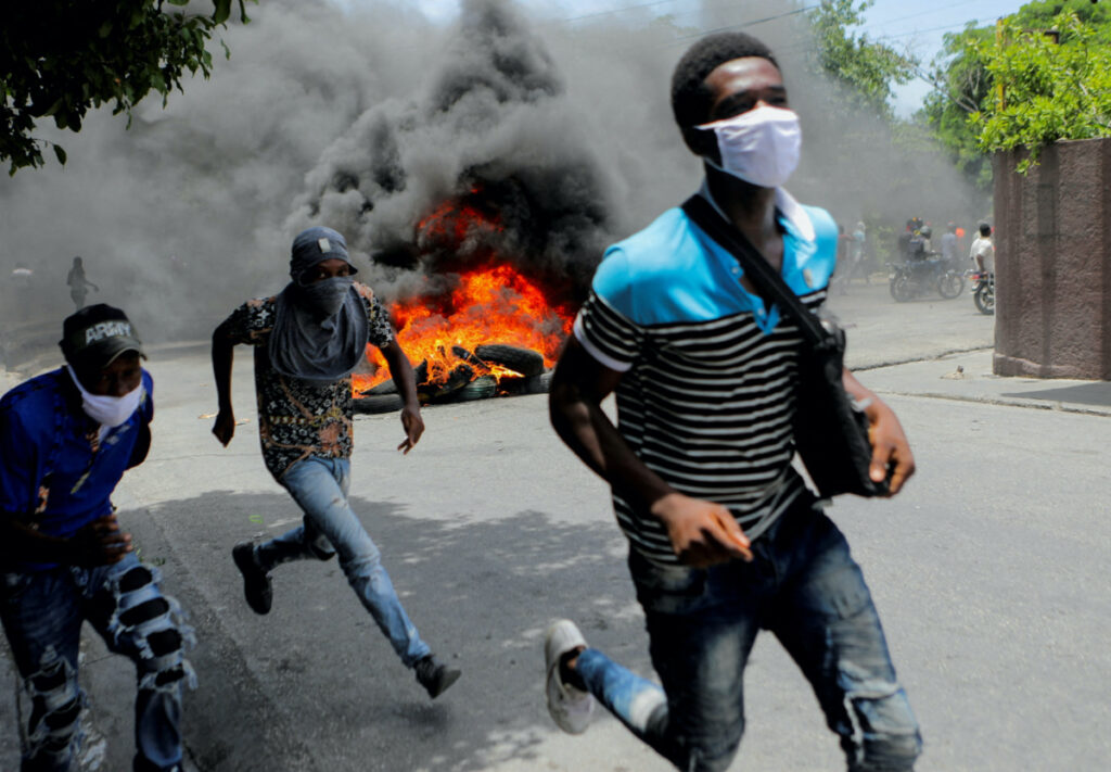 Men run next to burning tires during a protest demanding an end to gang violence, in Port-au-Prince, Haiti, on 14th August, 2023
