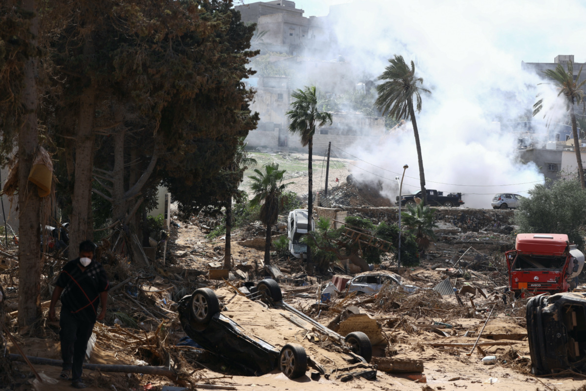 A man walks among rubble with smoke caused by a sanitation truck visible in the background among rising concerns of spread of infectious diseases after fatal floods in Derna, Libya, on 18th September, 2023.