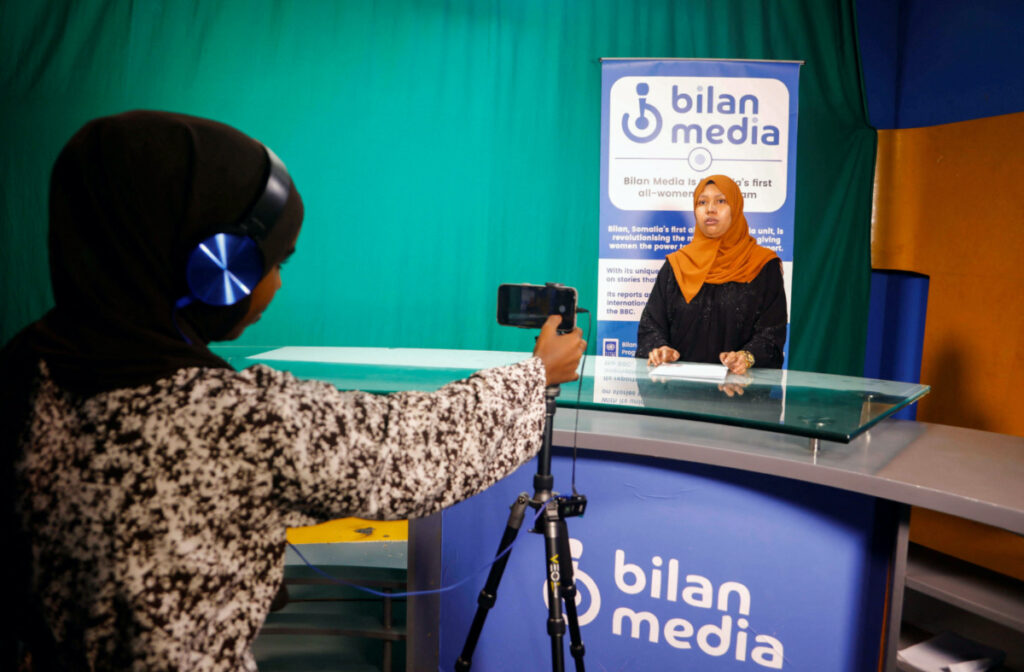 Shukri Mohamed Abdi and Fathi Mohamed Ahmed, journalists at Bilan Media, Somalia's first all-women media team, use a mobile to record the news inside the Bilan Media studios in Mogadishu, Somalia, on 20th August, 2023.