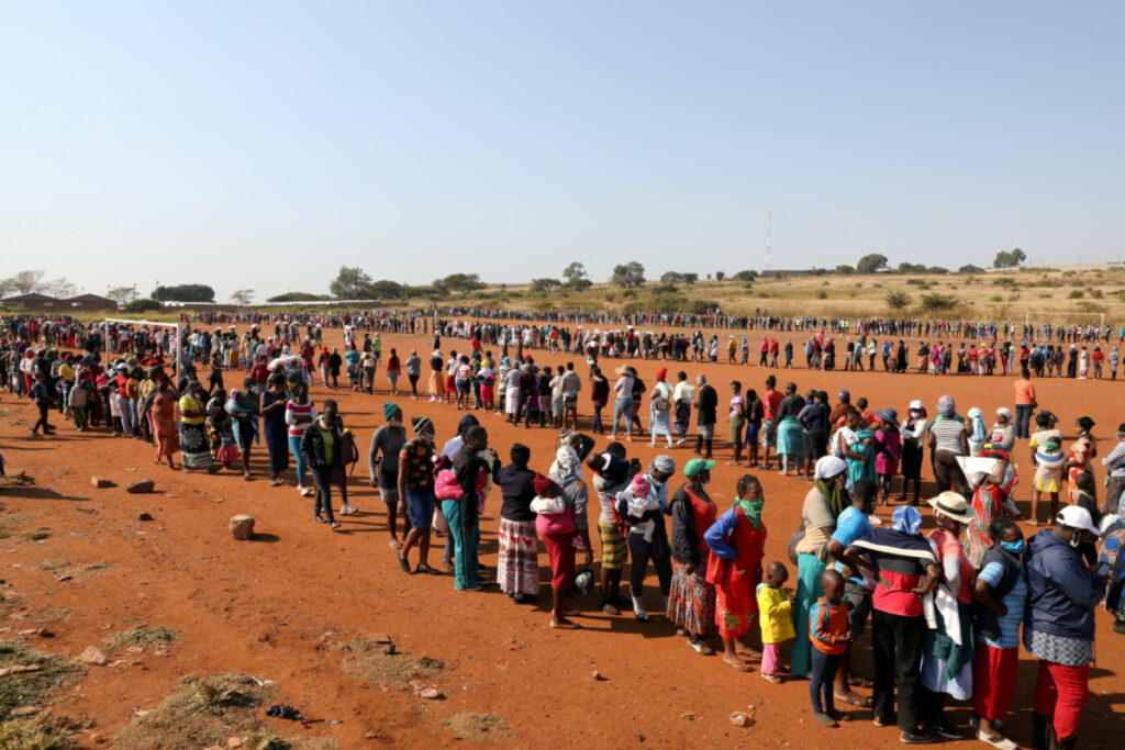 People stand in a queue to receive food aid, during the coronavirus disease outbreak at the Itireleng informal settlement, near Laudium suburb in Pretoria, South Africa, on 20th May, 2020
