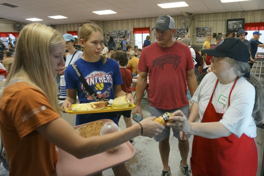 Volunteer Jane McClure, right, serves breakfast items at the Hamline Church Dining Hall to Jeff Knott and his two teenage daughters, Marin, left, and Elsie, during the Minnesota State Fair in Falcon Heights, Minnesota, on Thursday, 24th August, 2023