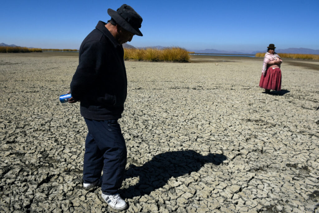 Gabriel Flores and Isabel Apaza walk on the dry, cracked bed near the shore of Lake Titicaca in drought season in Huarina, Bolivia, on 3rd August, 2023