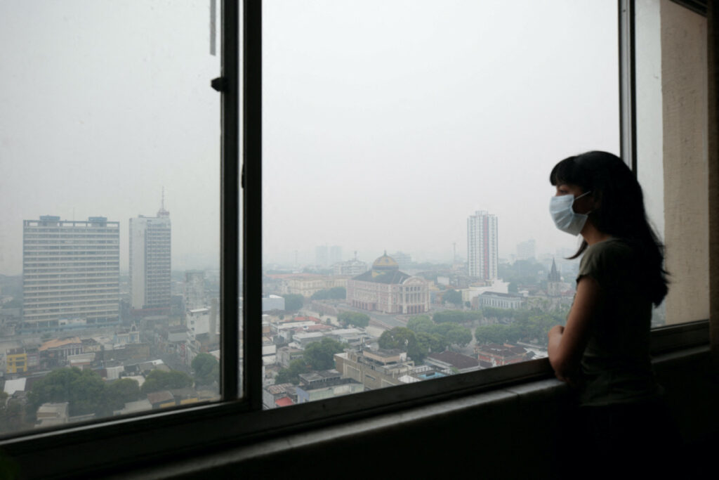 Journalist Indiara Bessa looks out from her apartment as smoke from wildfires in the Amazon is seen in Manaus, Brazil, on 12th October, 2023