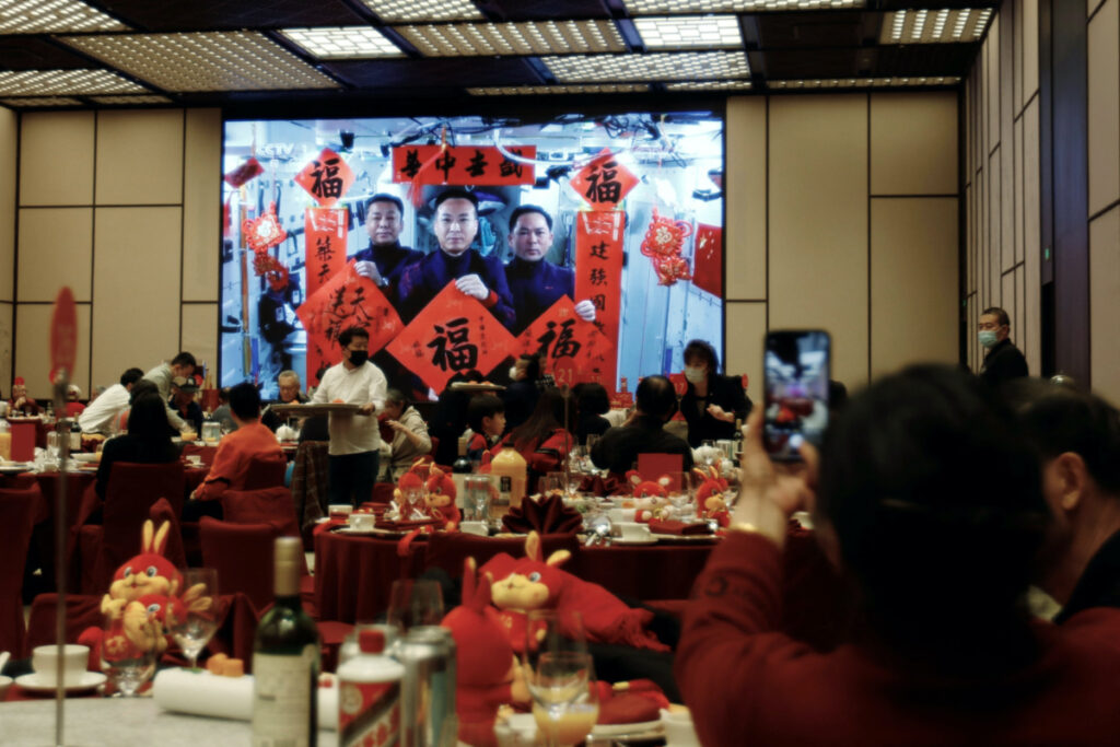 A woman takes pictures of a screen displaying the Spring Festival greetings by Chinese astronauts Fei Junlong, Deng Qingming and Zhang Lu from China's space station, during a Lunar New Year's Eve dinner service at Shangri-La Shougang Park hotel in Beijing, China, on 21st January, 2023.