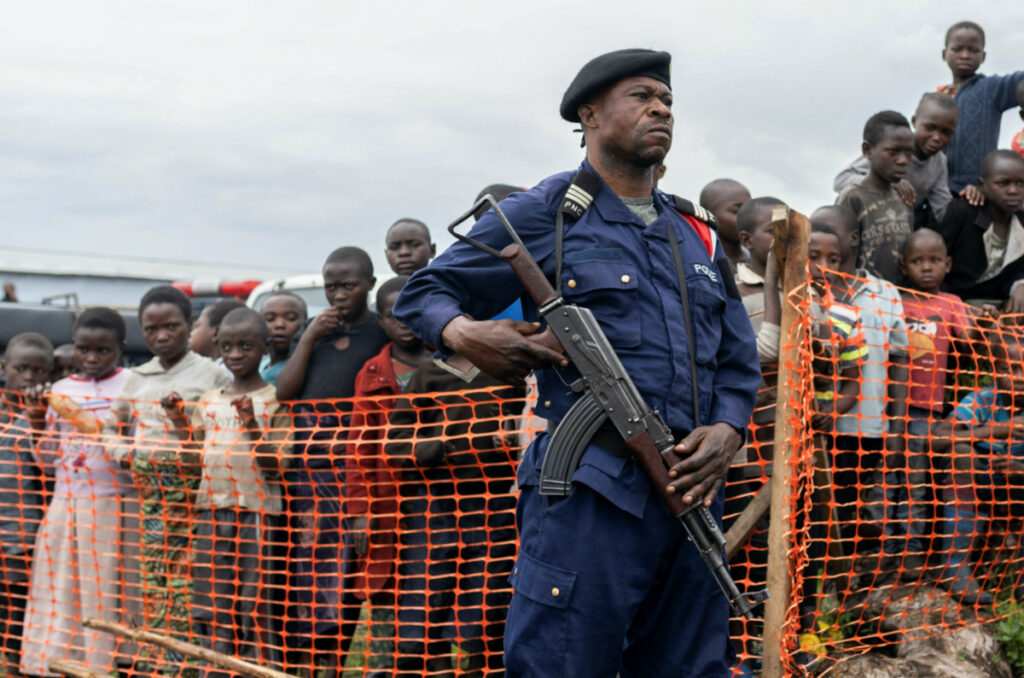 A Congolese police officer stands guard near internally displaced people gathered during the visit of a delegation of the UN Security Council at the Bushagara site near Goma in the North Kivu province of the Democratic Republic of Congo, on 12th March, 2023