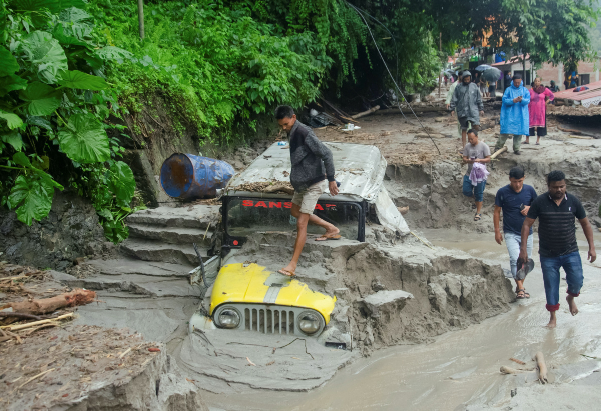 People walk along a street as a jeep is buried in the mud due to the flood at Teesta Bazaar in Kalimpong District, West Bengal, India, on 4th October, 2023.