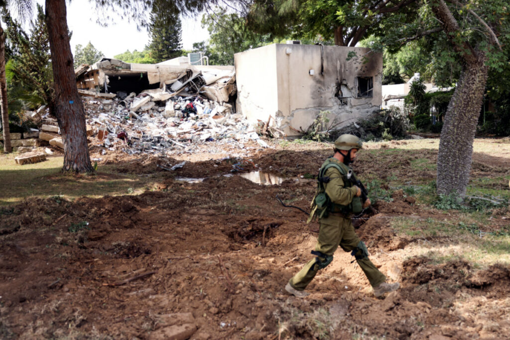 An Israeli soldier walks past a building damaged after rockets were fired from the Gaza Strip into Israel, in Kibbutz Kfar Aza, in southern Israel, on 10th October, 2023