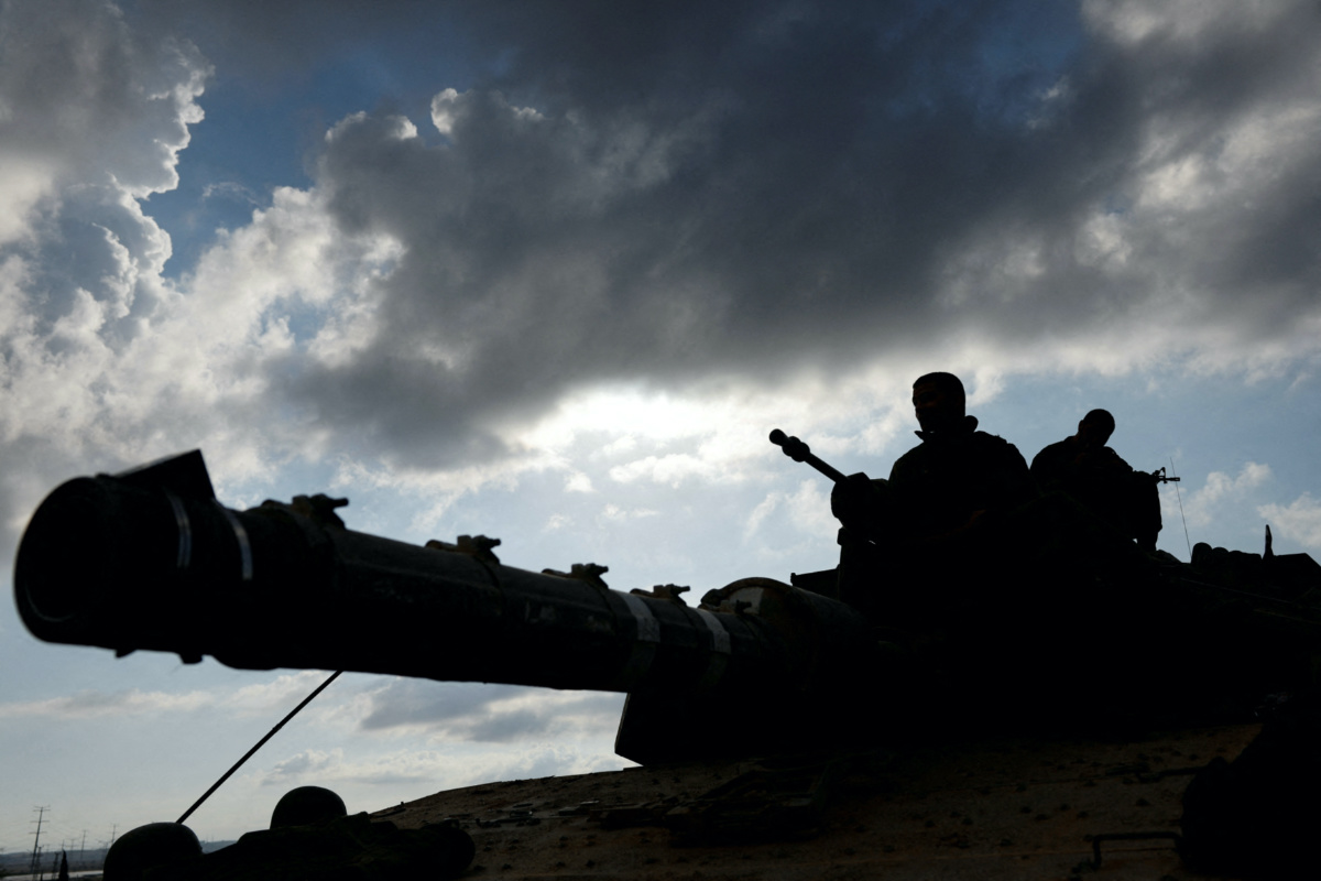 Israeli soldiers are silhouetted as they sit astride an Israeli tank near Israel's border with the Gaza Strip, in southern Israel, on 15th October, 2023