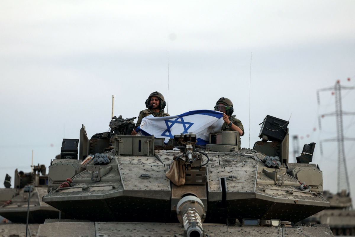 Israeli soldiers hold an Israeli flag while in a tank near Israel's border with the Gaza Strip, in southern Israel, on 12th October, 2023. 