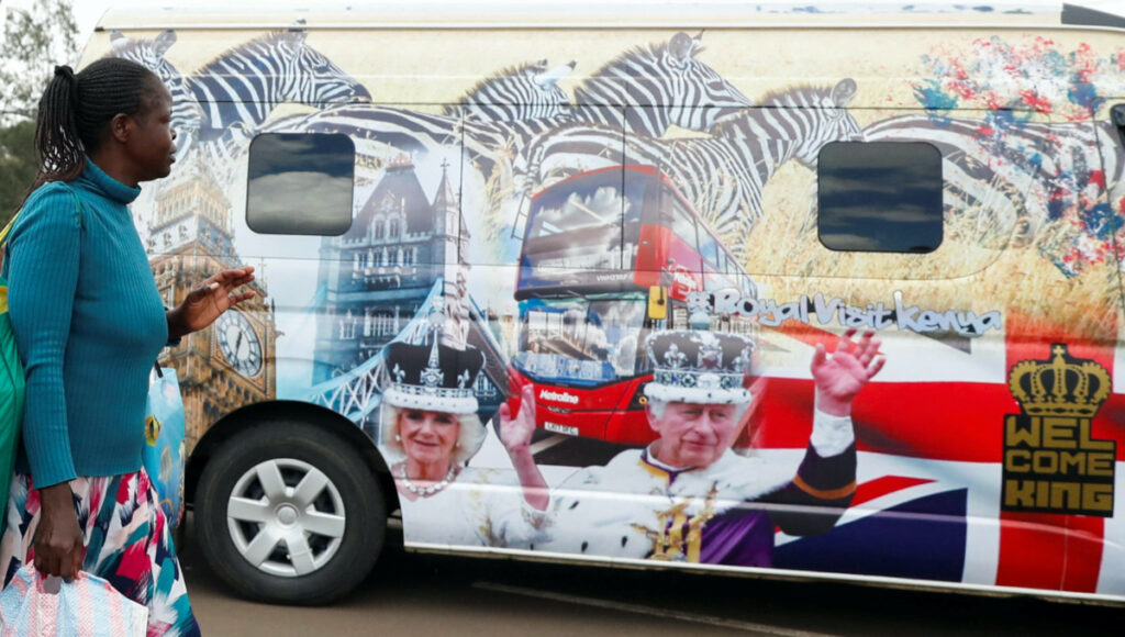 A woman gestures as she walks past a British High Commission courtesy van decorated with images of Britain's King Charles III and Queen Camilla ahead of their state visit, at the Green Park bus terminus in Nairobi, Kenya, on 27th October, 2023