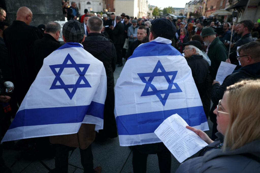 A man wrapped in the Israeli flag stands as a woman holds the text of prayer during multi-confessional prayer for peace after gunmen from Hamas entered Israeli territory on Saturday, at Old Town in Warsaw, Poland, on 13th October, 2023.