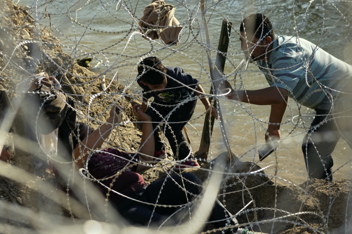 Migrants who crossed the Rio Grande from Mexico to the US work their way through concertina wire, on Friday, 22nd September, 2023, in Eagle Pass, Texas, US.