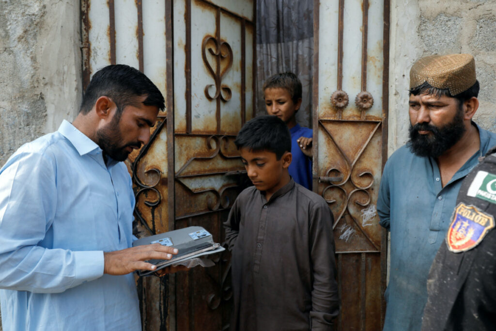 A worker from the National Database and Registration Authority, speaks to residents while verifying their identity cards on an online tab, during a door to door search and verification drive for undocumented Afghan nationals, in an Afghan Camp on the outskirts of Karachi, Pakistan, on 21st November, 2023.