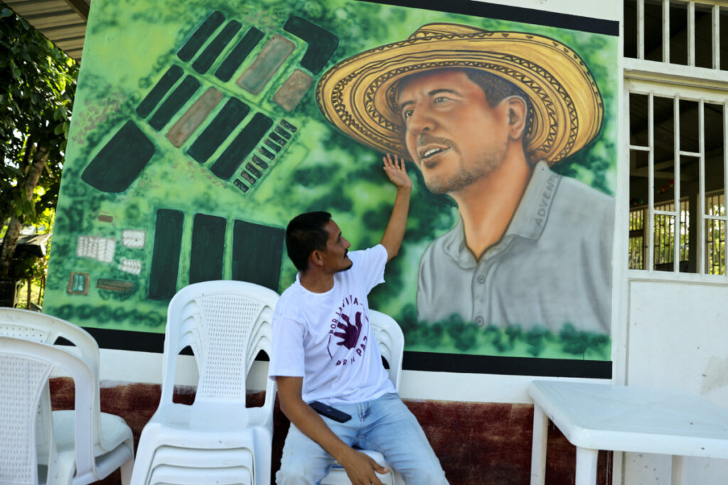 Armando Aroca, environmentalist, former guerrilla and signatory of the peace agreement between the Revolutionary Armed Forces of Colombia and the Colombian government, and current nursery manager of the Common Community Multi Active Cooperative farm, points to a mural with the image of Jorge Santofimio, a murdered environmentalist and former guerrilla member and signatory of the peace agreement between the Revolutionary Armed Forces of Colombia and the Colombian government, in Puerto Guzman, Colombia on 27th June, 2023