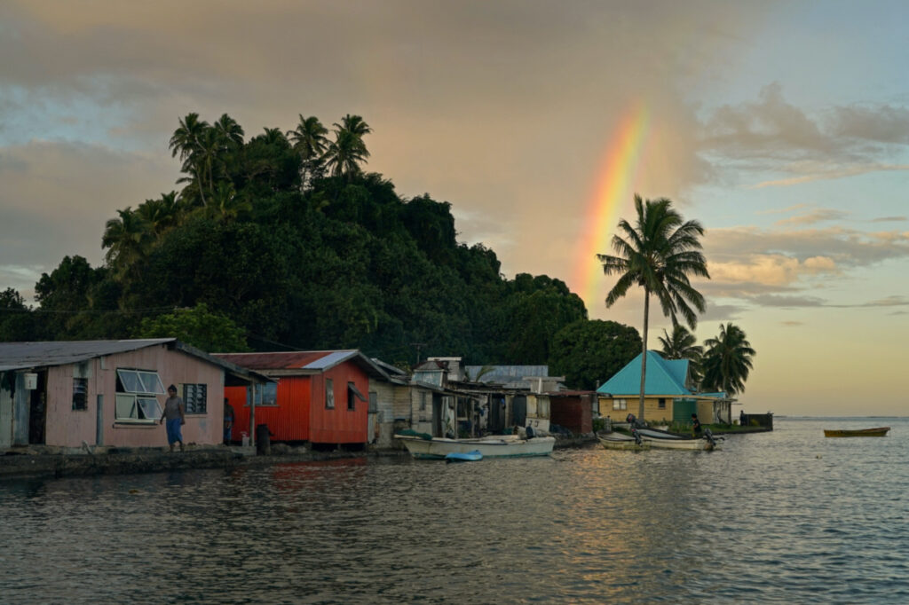 Local resident Tarusila Boseiwaqa walks along a sea wall that no longer protects homes from the intrusion of water at higher tides, as a rainbow forms over Serua Village, Fiji, on 14th July, 2022.