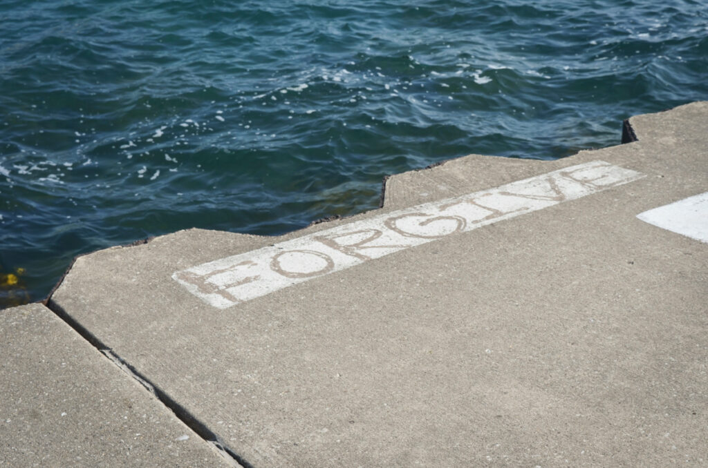 “Forgive” painted on the sidewalk beside a body of water