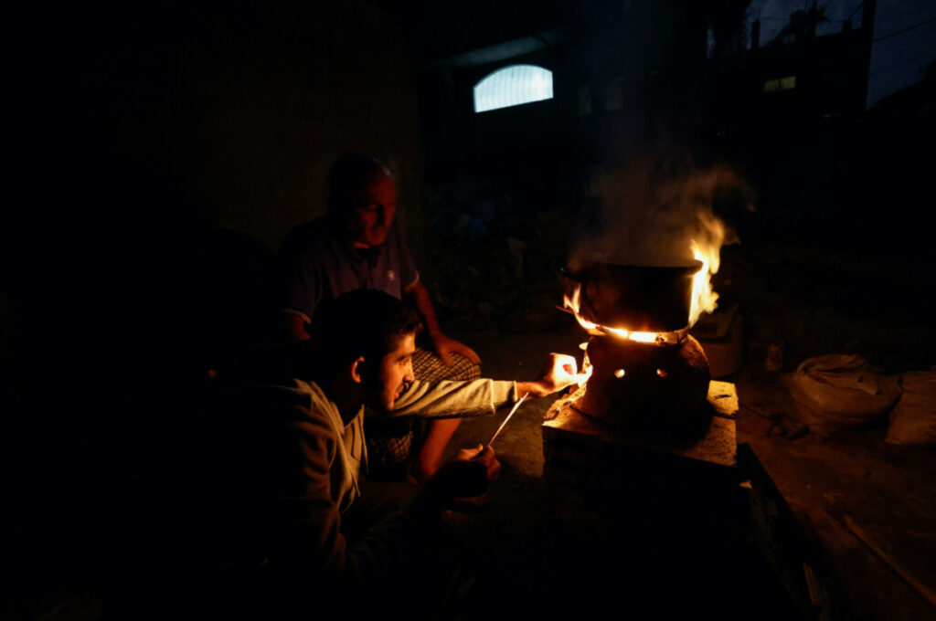 Palestinians sit next to a fire near the rubble of a house hit in an Israeli strike during the conflict, amid a temporary truce between Hamas and Israel, in Khan Younis in the southern Gaza Strip on 25th November, 2023.