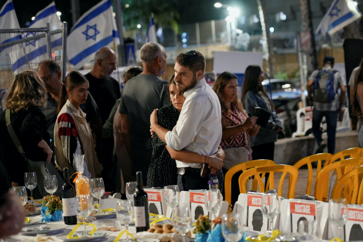 An Israeli couple embraces behind a Shabbat dinner table set for the hostages and the missing at an event held for families, friends and supporters, in Tel Aviv, Israel, on 10th November, 2023. 