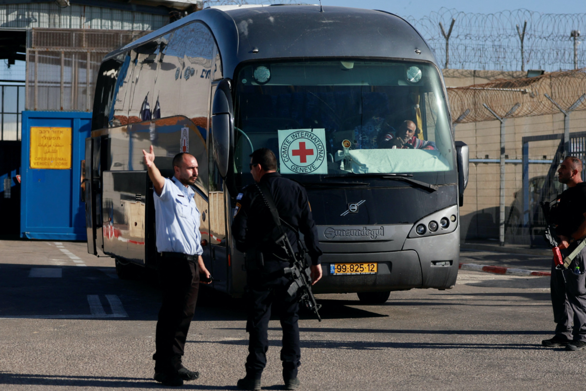 Israeli military personnel stand near a Red Cross bus outside the Israeli military prison, Ofer, near Ramallah, in the Israeli-occupied West Bank, from another Israeli prison, before they are due to be released as part of a deal between Israel and Palestinian Islamist group Hamas, to free hostages held in Gaza in exchange for the release of Palestinian prisoners, on 24th November, 2023.