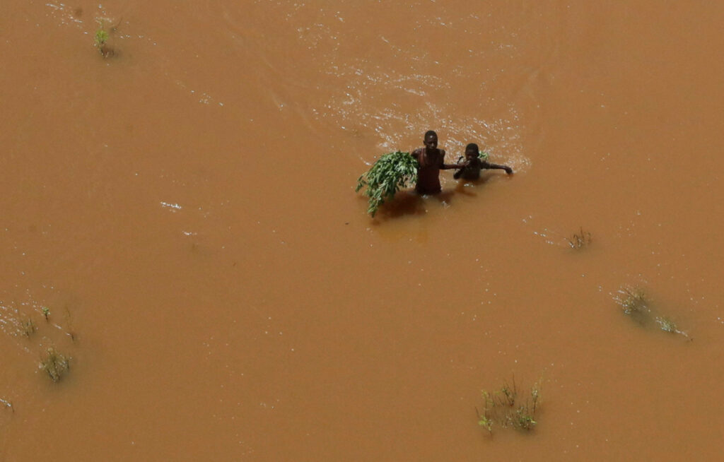 People hold on to plants as they wade through flood waters after they were displaced following heavy rains in Garsen, Tana Delta within Tana River county, Kenya, on 23rd November, 2023.